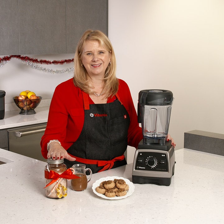 Woman standing next to blender with homemade chocolate sauce and cookies on kitchen counter